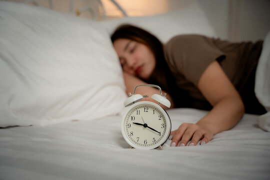 Insomnia concept of a young woman using a smartphone while lying awake in bed at night beside an alarm clock, showing sleeplessness, insomnia, smartphone, bedtime, sleep, fatigue