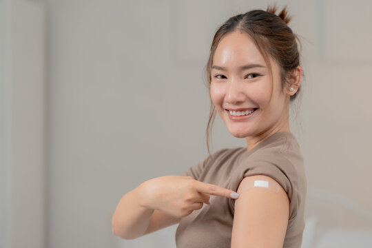 Vaccination, immunization and prevention concept. Smiling young Asian woman points to a bandage on her upper arm after receiving a vaccine. Vaccine, immunity, healthcare, protection