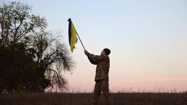 Male military waving blue-yellow banner on liberated territory occupied by russia. Young soldier of ukrainian army lifted flag of Ukraine in honor of victory against russian aggression at dusk