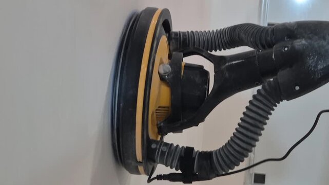 Side view video along the wall of a drywall sander machine moving up and down sanding the painted wall.