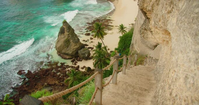 Looking down stone steps toward sandy shore with large rocky cliffs and ocean waves