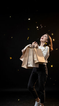 A young woman ecstatically holding shopping bags amidst falling confetti.