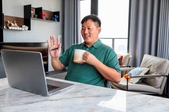 Smiling man waving during a laptop video call.