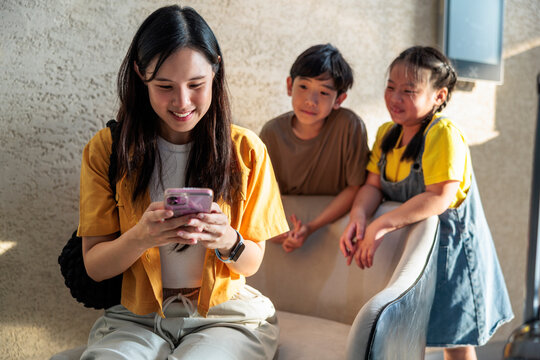 Woman shows smartphone screen to two curious children.