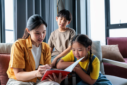 A mother helps two children with schoolwork at home.