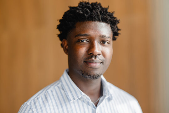 Young Man With Short Curly Hair Poses Indoors by Wooden Backdrop