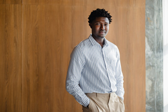 Man in a Striped Shirt Stands Against a Wooden Wall