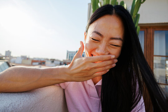 Woman laughing outdoors covering mouth with hand