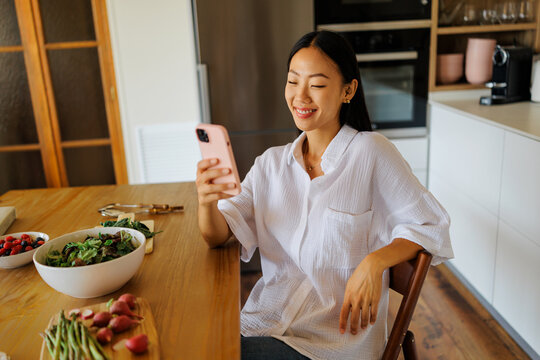 Woman browsing smartphone at kitchen table with fresh food