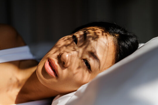 Woman laying in bed with dappled sunlight shadows on face