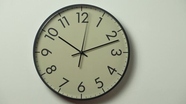 Modern black wall clock time lapse on white wall. Analog clock hands showing 10:10 and passing time.