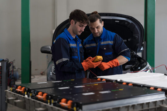 Electric vehicle car services. EV car. Diagnostic battery pack. Team of technician or Mechanic wearing protective gloves diagnosing electric car vehicles battery, component checks at auto workshop