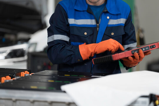 High-voltage battery checks, maintenance. Technician or Mechanic wearing protective gloves diagnosing electric car vehicles battery, component checks at auto workshop. Software updates