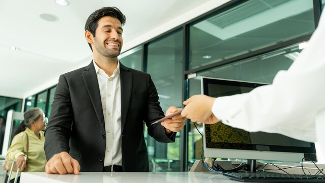 Smiling business traveler receives a boarding pass from airport staff at a modern check-in counter with digital technology in the terminal.