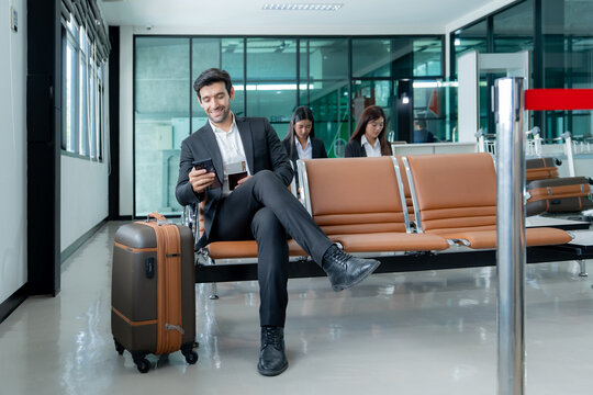 Business traveler uses a smartphone while waiting at an airport terminal with luggage reflecting modern business travel and mobile connectivity