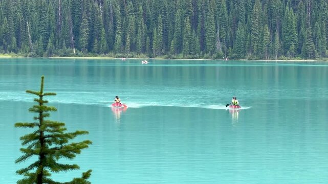 Emerald Lake, Canada - August 14, 2026: Visitors paddling canoes across the turquoise waters of Emerald Lake in Yoho National Park, surrounded by the Canadian Rocky Mountains.