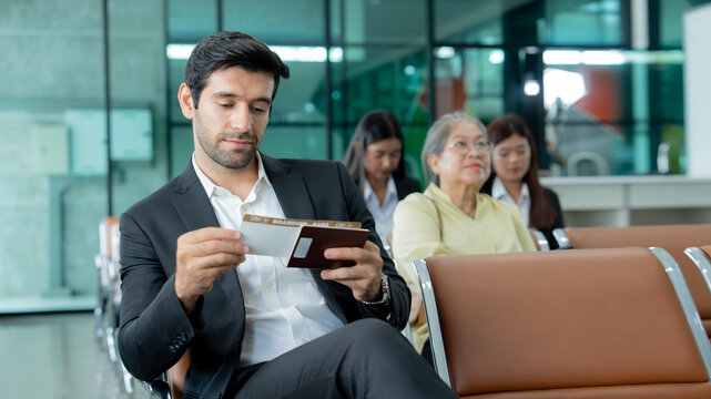 Business traveler checks his boarding pass and passport while waiting at an airport terminal representing corporate travel and professional mobility.