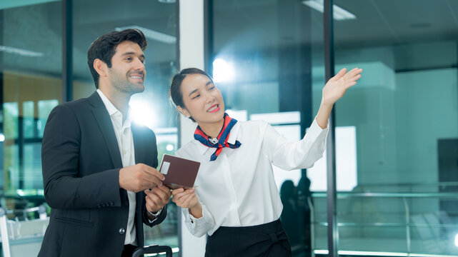 A female service agent assists a passenger with travel information while he carries a tablet and pulls his luggage through the terminal.
