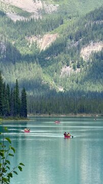 Emerald Lake, Canada - August 14, 2026: Visitors paddling canoes across the turquoise waters of Emerald Lake in Yoho National Park, surrounded by the Canadian Rocky Mountains.
