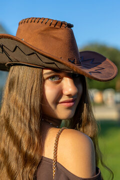 Close-Up Portrait of Young Girl in Brown Cowboy Hat. Young girl in a brown cowboy hat smiles in a sunlit outdoor close-up portrait.