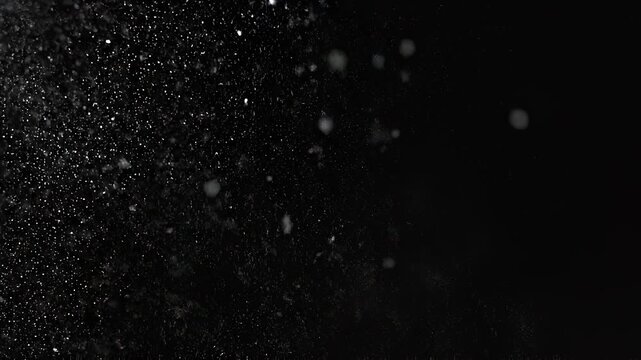 Fine white powder particles dispersing slowly in darkness with subtle motion and bokeh effects
