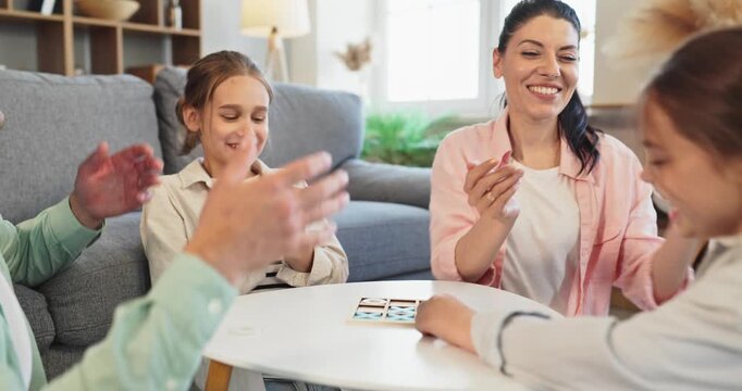 Family parents children playing boardgame together at home. They and the kids enjoy a fun strategy game around a small table in a cozy room. Strong family bonding and quality time concept.