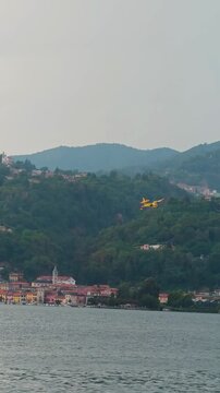 Firefighting Canadair aircraft flying over Italian lake during large forest wildfires, preparing to scoop water, supporting aerial firefighting operations and wildfire suppression in Europe. 4K video