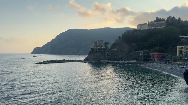 4K video of Monterosso al Mare in Cinque Terre, Italy, during a dramatic summer evening, featuring rows of beach chairs and umbrellas, the Ligurian Sea, colorful coastal buildings, and the rugged hill