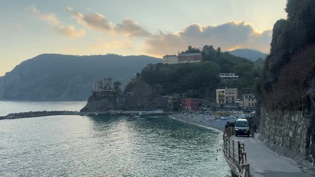 4K video of Monterosso al Mare in Cinque Terre, Italy, during a dramatic summer evening, featuring rows of beach chairs and umbrellas, the Ligurian Sea, colorful coastal buildings, and the rugged hill