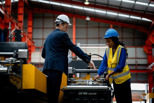professional engineer, worker, technician use clipboard discuss work, walk in steel metal manufacture factory plant industry. Black African American man and woman wear hard hat check quality machine