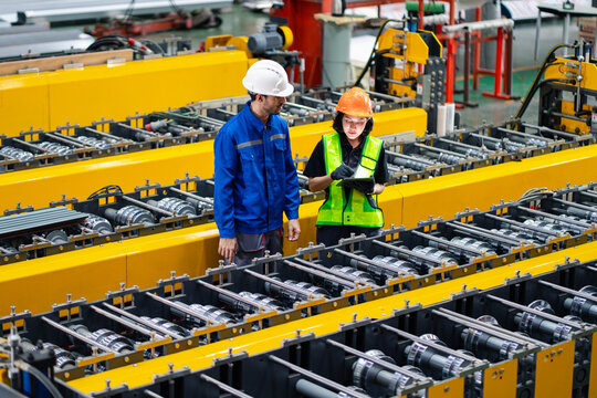 professional engineer,worker,technician use clipboard discuss work, walk in steel metal manufacture factory plant industry. Black African American man and woman wear hard hat check quality machine.