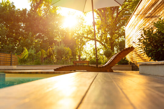 Elegant Wooden Lounge Chairs with White Umbrella at Poolside During Sunset. Concept of luxury and comfort in a serene outdoor setting