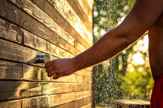 Man enjoying outdoor shower at sunset. Concept of summer rest, fun, and relaxation with flowing water