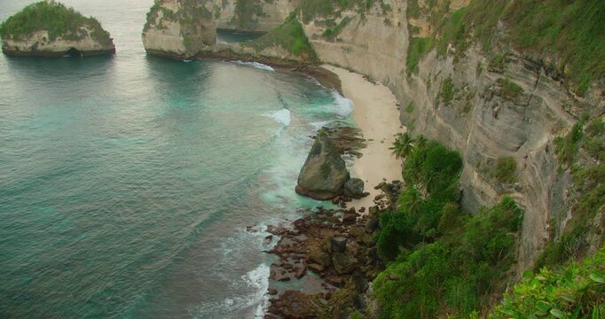 Top view of limestone cliffs and turquoise ocean water on tropical beach with palm trees