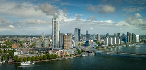 Panoramic view of Rotterdam skyline and the Nieuwe Maas river under dramatic clouds and blue sky, featuring modern high-rise architecture. © Jonas Weinitschke