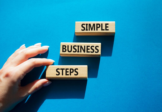 Simple business steps symbol. Concept words simple business steps on wooden blocks arranged as steps. Business planning concept. Businessman hand arranging wooden blocks. Blue background. Copy space.