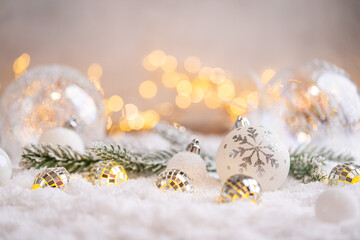Naklejka premium A Christmas background featuring textured white and gold baubles alongside tiny mirror disco balls and frosted pine on snow, softly lit by warm twinkling lights with copy space.