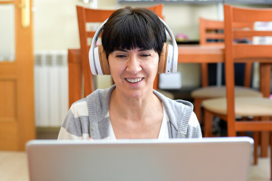 Relaxed woman with headphones enjoying cheerful conversation through her laptop at cozy cafe