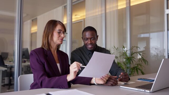 Business woman and man discussing document together, laughing, open office. Coach and Employee review report laughing together, leading cross-functional projects, expanding professional network.