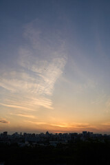 Obraz premium Colorful Sunset Sky Glowing Above Dark City Skyline With Wispy Clouds Over Distant Buildings At Evening.