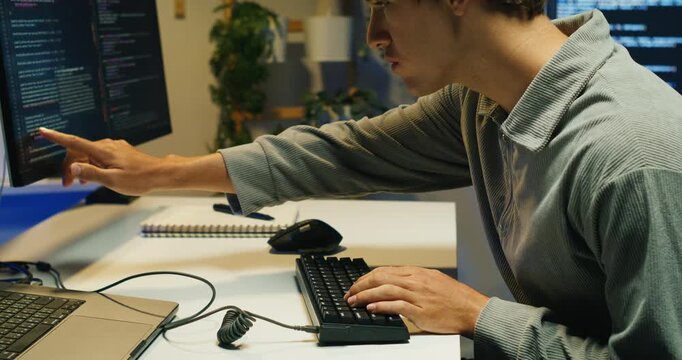 A male programmer writes and tests code at a workstation beside server racks, focusing on database calls.