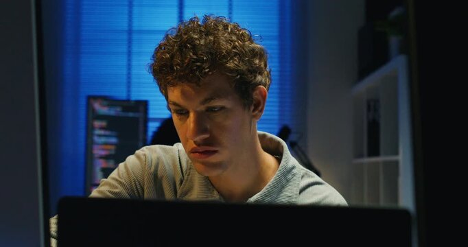 A young Caucasian developer analyzes server logs by monitor light to diagnose a network issue.