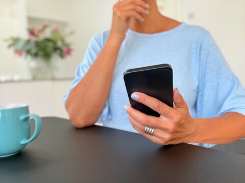 Close-up of a confused woman sitting in a living room looking at her mobile phone