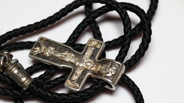 A small silver cross hangs from a black cord with a silver bead, suitable for various occasions and faith-based scenes. Rotating in a circle