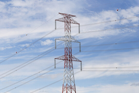 High voltage electricity transmission tower. Power lines across blue sky. Steel lattice pylon and cables. Electrical grid across open landscape. Energy distribution forms industrial background.