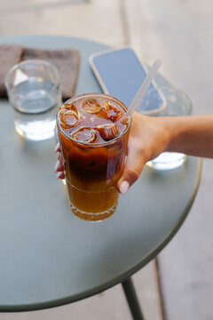 Close-up of a young Woman sitting at a table outdoors drinking an Iced Bumble Coffee drink on a summer day
