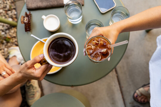 Overhead view of two woman sitting at an outdoor cafe toasting with an iced bumble coffee and an americano coffee