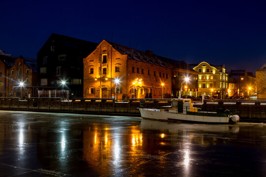 View into land of a boat moored in a frozen river on a winter night, Klaipeda, Lithuania