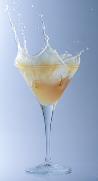 Close-up of an ice cube splashing into a yellow fruit juice in a cocktail glass