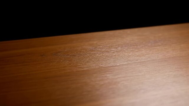 Warm honey amber wooden tabletop with subtle focus shift, shifting highlights, varnished grain, diagonal perspective, deep black background, smooth studio lighting